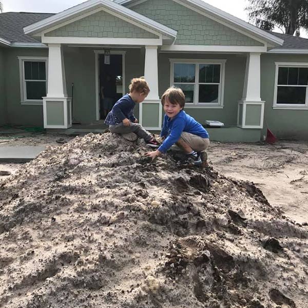 Two children playing on the top of a large dirt pile in front of a house