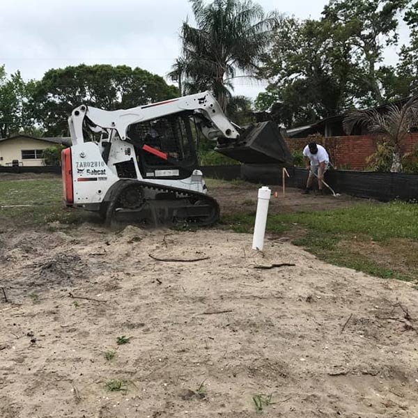 Work site with Bobcat & man scooping dirt with a shovel